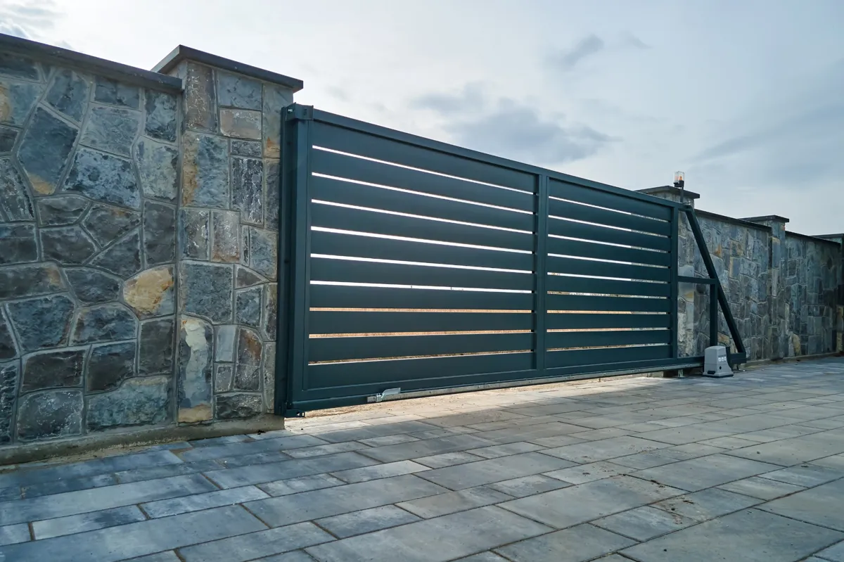 Portail automatique en métal, intégré dans un mur en pierre, installé dans une propriété résidentielle.